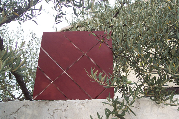 Œuvre en ciment rouge de Christiane Colmagro, photographiée en extérieur parmi les oliviers.